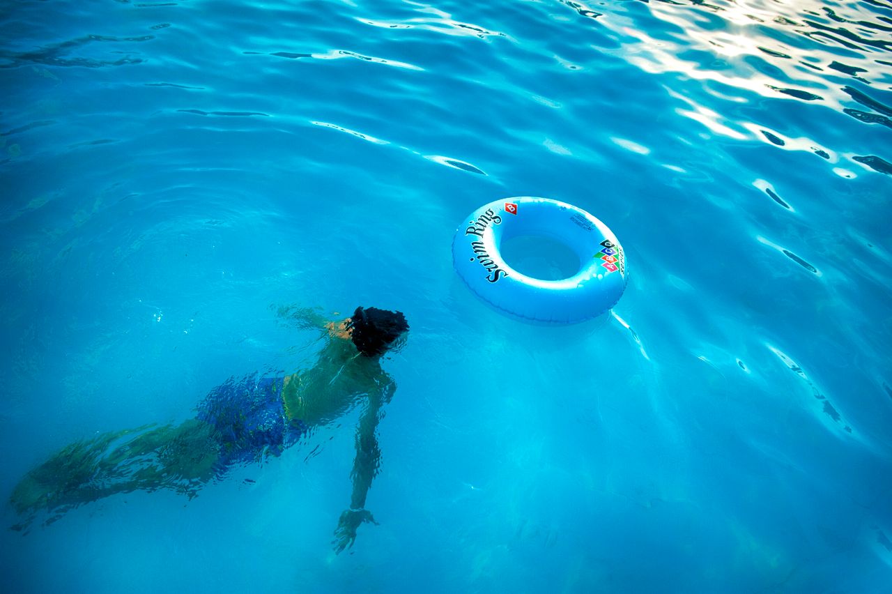 An individual swims underwater in a bright pool beside a floating swim ring.